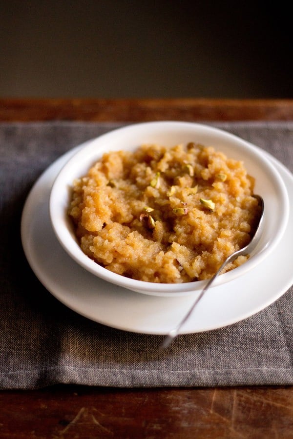 moong dal halwa served in a white bowl kept on a white plate with a spoon inside the bowl. 