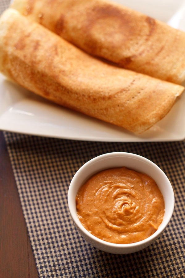 onion tomato chutney served in a small white bowl with a platter of dosas kept on the top side.