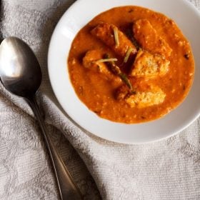 overhead shot of paneer makhani in a white bowl with a silver spoon and grey and white napkin.