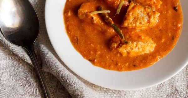 overhead shot of paneer makhani in a white bowl with a silver spoon and grey and white napkin.