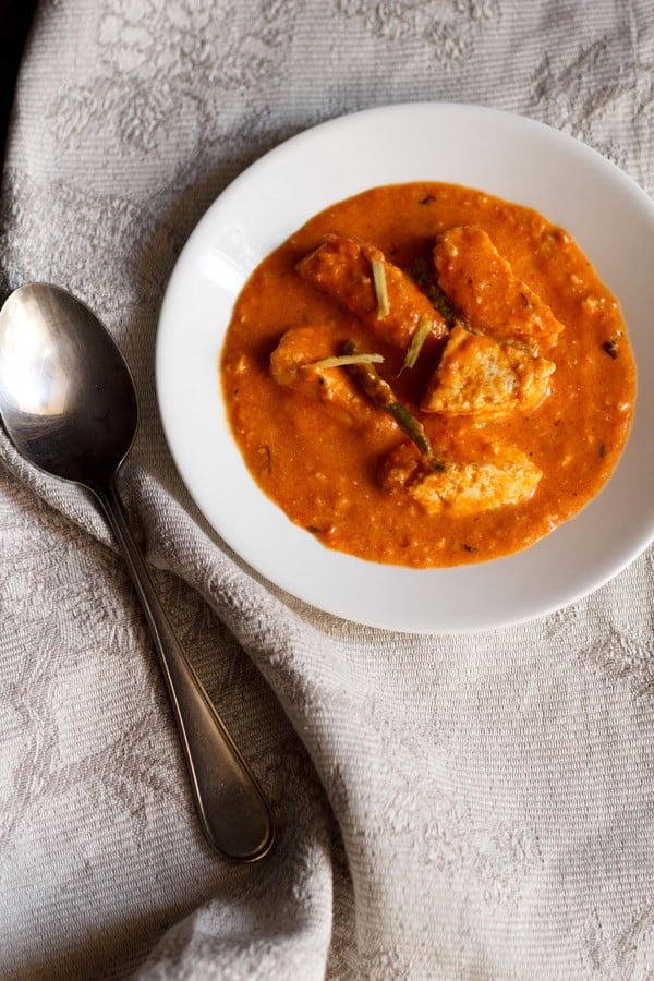 overhead shot of paneer makhani in a white bowl with a silver spoon and grey and white napkin.