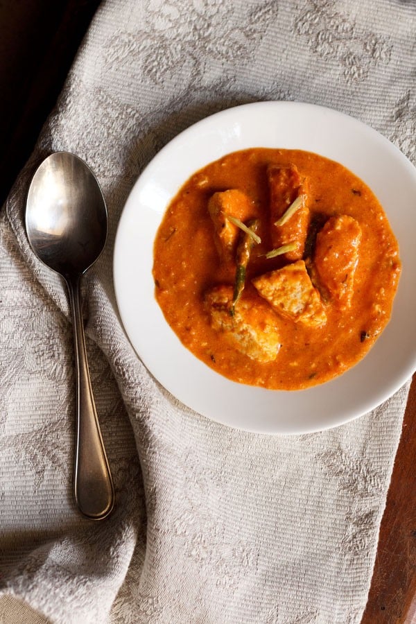 overhead shot of paneer makhani in a white bowl with a silver spoon and grey and white napkin