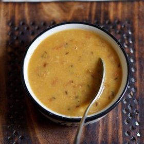 arhar dal served in a black rimmed bowl with a spoon in it.