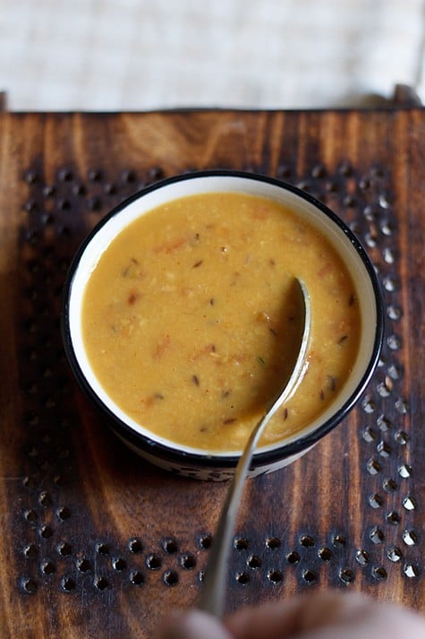 arhar dal served in a black rimmed bowl with a spoon in it.
