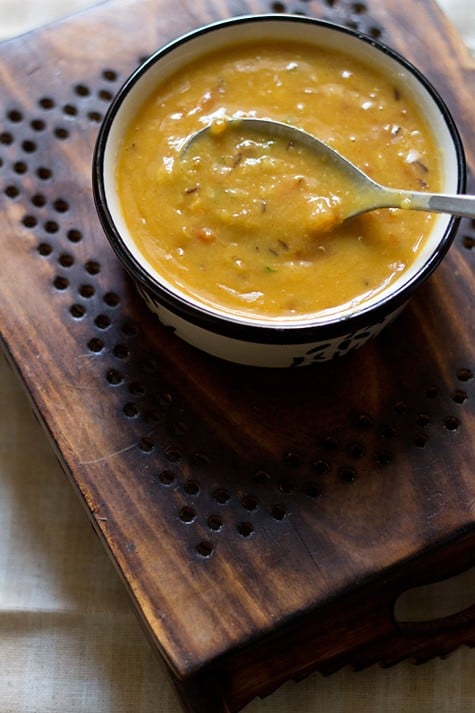 toor dal served in a black rimmed bowl with a spoon in it. 