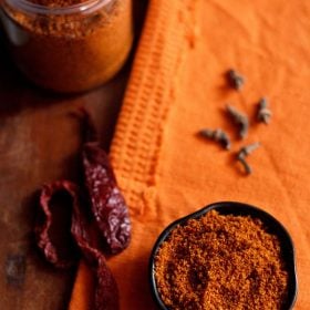 bisi bele bath powder served in a small black bowl with whole spices in the background.