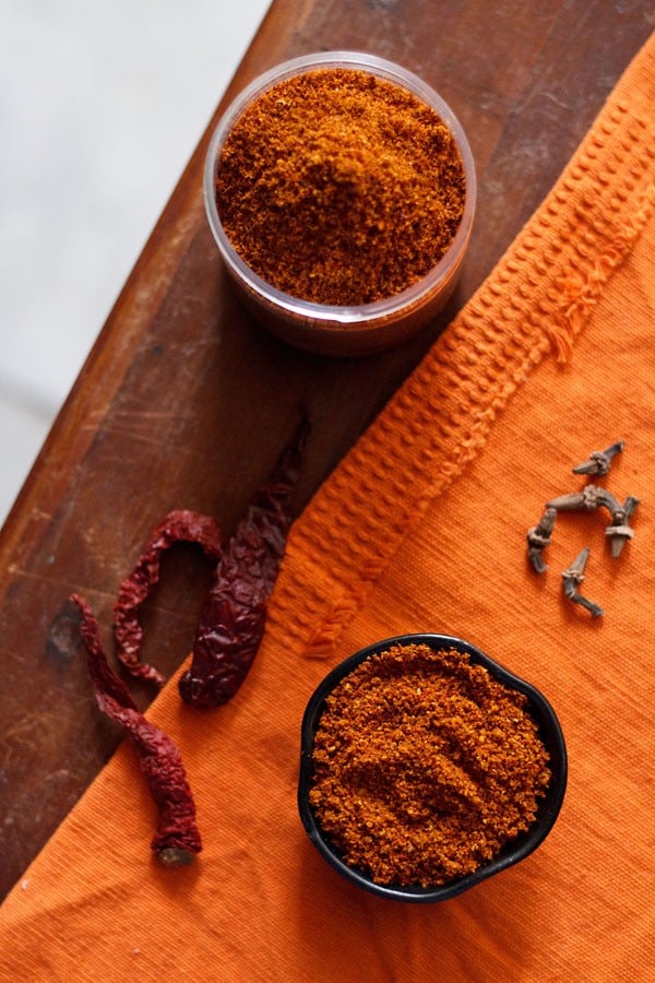 bisi bele bath powder in a small black bowl and jar with whole spices in the background. 