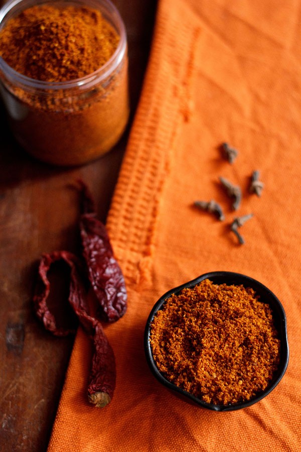 bisi bele bath powder served in a small black bowl with whole spices in the background.