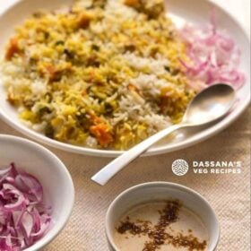 burani raita sprinkled with roasted cumin powder and served in a small bowl with a plate of veg biryani and a bowl of onion slices in the background and text layovers.