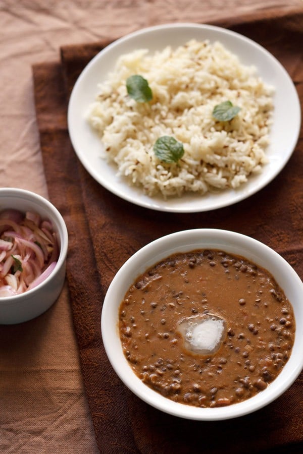 dal bukhara served in a bowl with butter on top, with jeera rice and onion salad 
