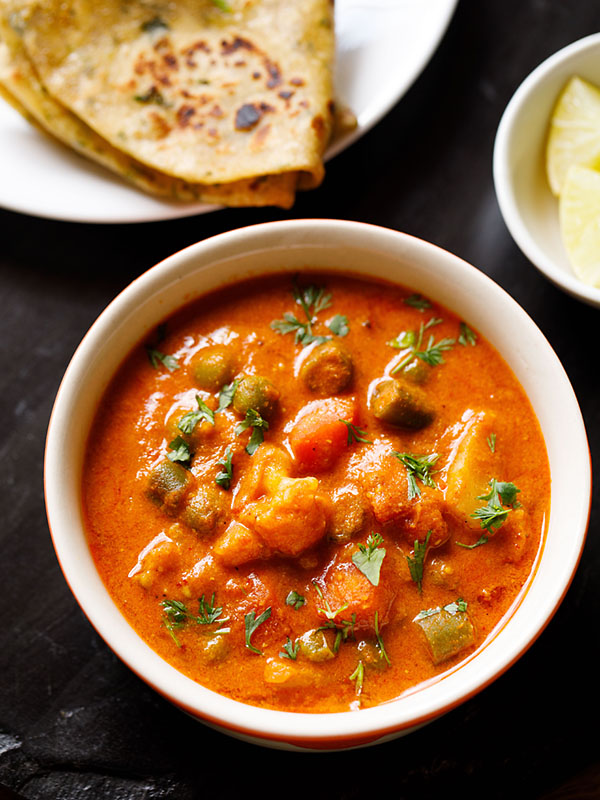 instant pot korma served in an off-white bowl with a plate of Indian flatbreads and a bowl of chopped lemons on a black slate board