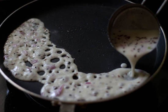 spreading onion rava dosa batter on pan. 