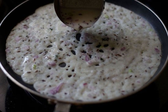 spreading onion rava dosa batter on pan. 