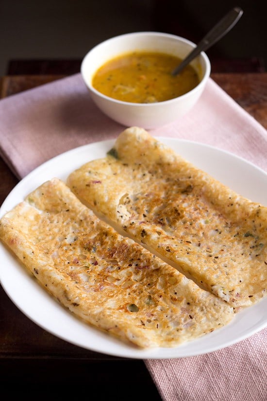 onion dosa served on a white plate with a side of sambar.