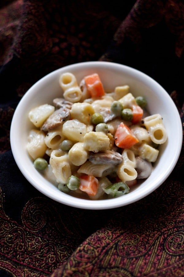 béchamel sauce veggie pasta served in a white bowl on a black printed cloth