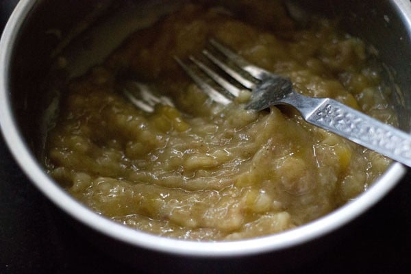 Silver fork mashing overripe bananas in bowl