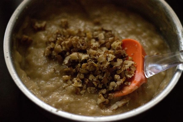 Orange spatula folding crushed walnuts into cake batter