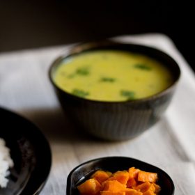 turmeric pickle in a small black bowl with a side of rice and curry