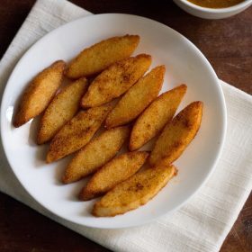 fried idli served on a white plate with a bowl of sambar kept on the top right side.