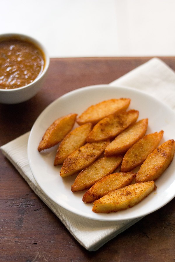 fried idli served on a white plate with a bowl of sambar kept on the top left side. 