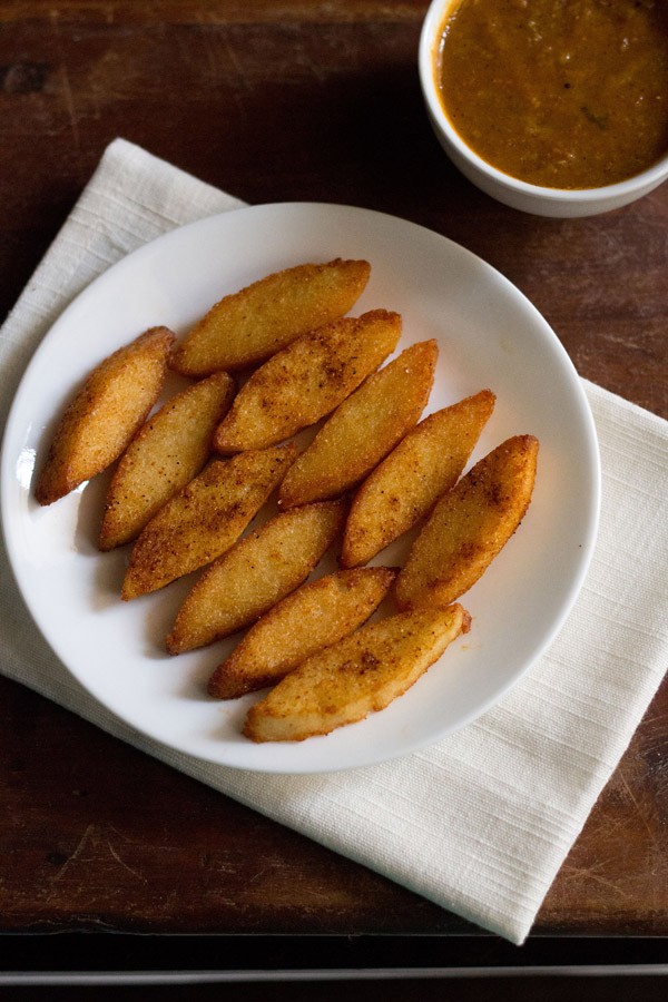 fried idli served on a white plate with a bowl of sambar kept on the top right side.