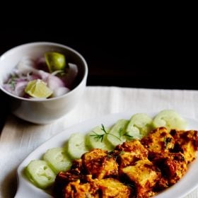 malai paneer served on a white platter with cucumber slices kept on left side on the platter, a bowl of onion and lemons.