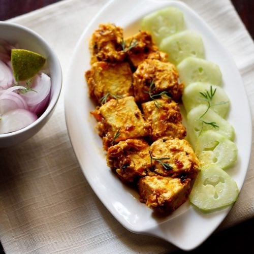 malai paneer served on a white platter with cucumber slices kept on left side on the platter, a bowl of onion and lemon.