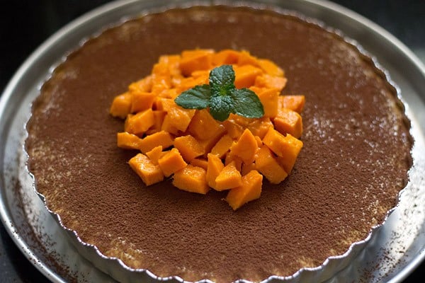mango cheesecake topped with cocoa powder, fresh mango chunks, and a sprig of mint.
