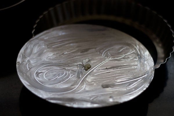 greasing a tart pan for making mango cheese cake recipe.