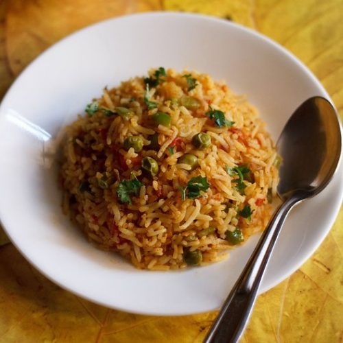 tawa pulao garnished with coriander leaves and served on a white plate with a spoon kept on the right side.