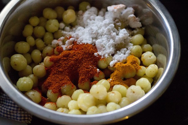 Adding red chili powder, turmeric powder, and rock salt to star gooseberries. 