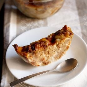 a thick round slice of bread butter pudding in a white plate with a spoon.