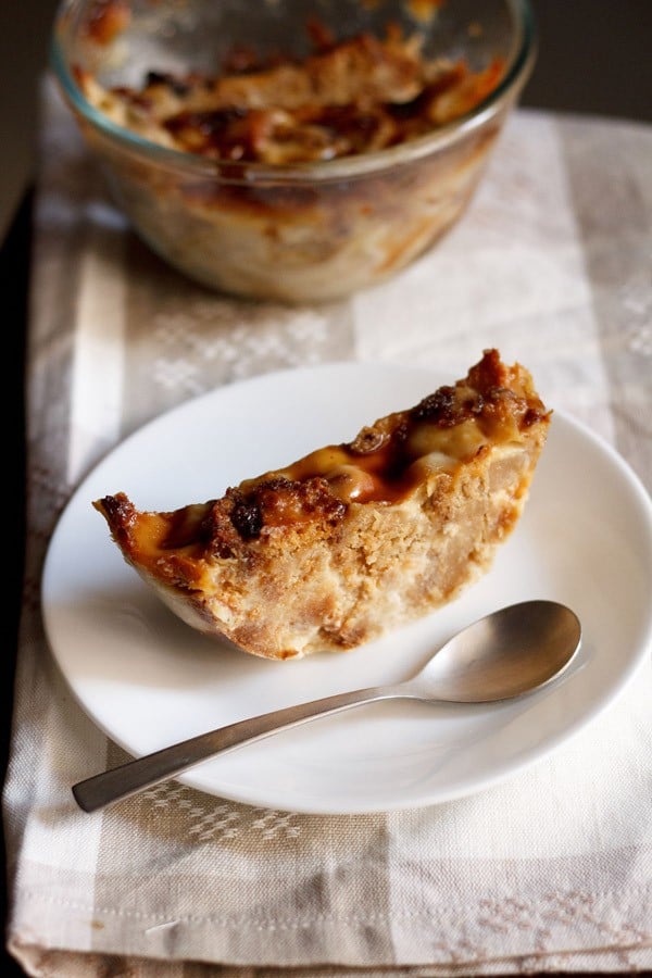 a thick round slice of bread butter pudding in a white plate with a spoon.