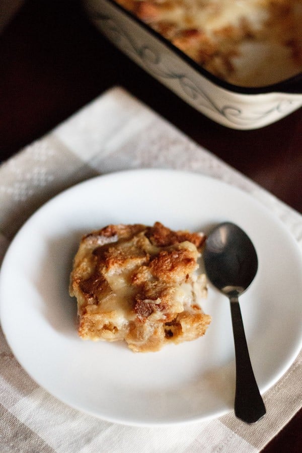 slice of eggless bread and butter pudding on a white plate with a silver spoon.