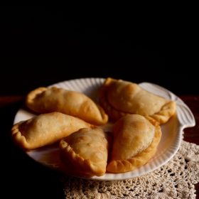 five karanji pieces on a white plate on a cream doily