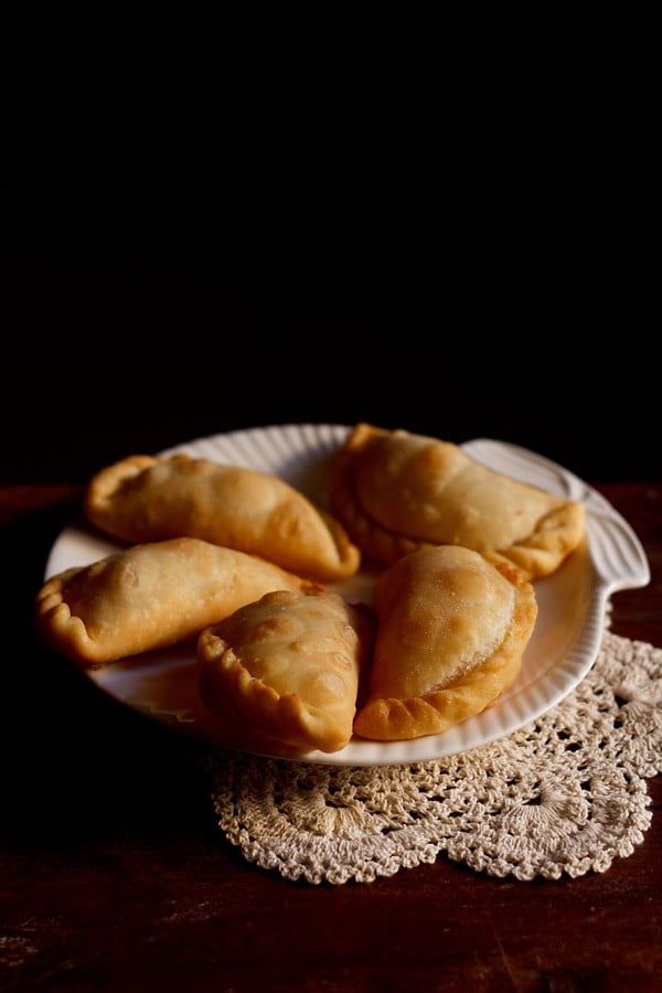 five karanji pieces on a white plate on a cream doily