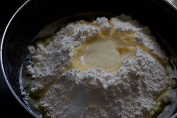 In a bowl or pan, take the flour and add ghee in the center