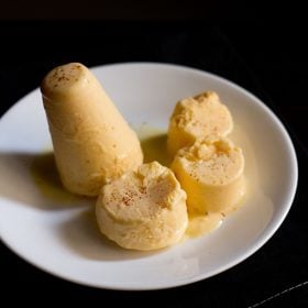 mango kulfi sliced and whole on a white plate on a dark brown napkin