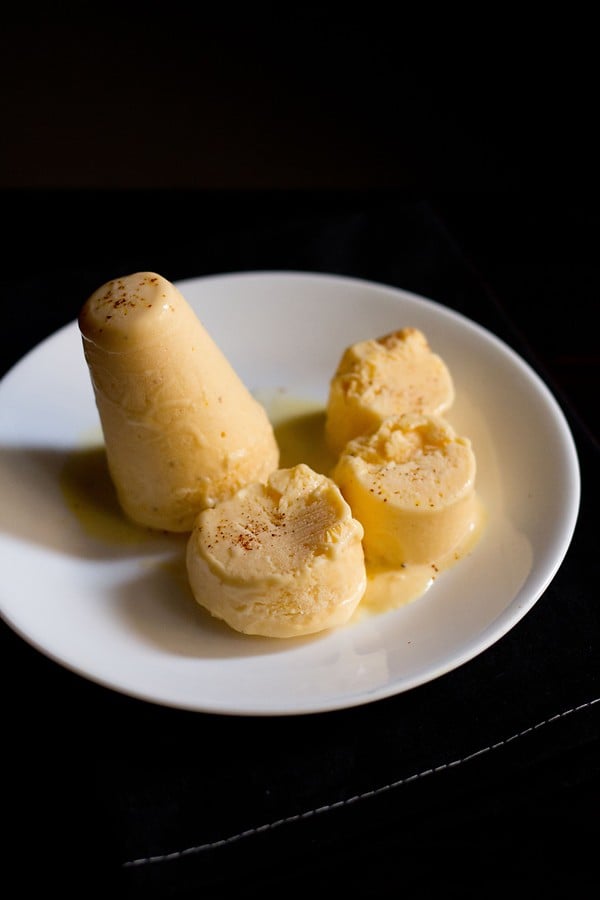 mango kulfi sliced and whole on a white plate on a dark brown napkin