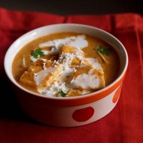 paneer makhanwala topped with cream, grated paneer, cilantro in an orange dotted bowl on a red cotton napkin