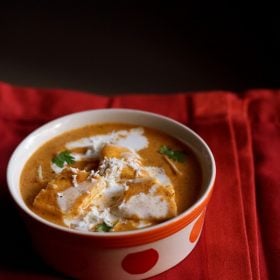 paneer makhanwala topped with cream, grated paneer, cilantro in an orange dotted bowl on a red cotton napkin