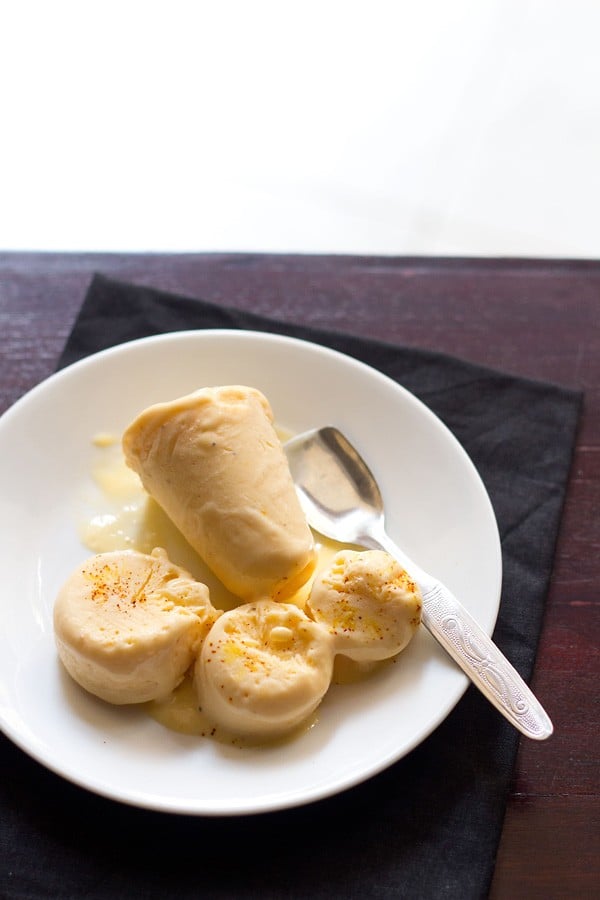 mango kulfi sliced and whole on a white plate with a steel spoon 