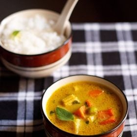 thai yellow curry served in a black rimmed ceramic bowl with a bowl of steamed rice kept in the background.