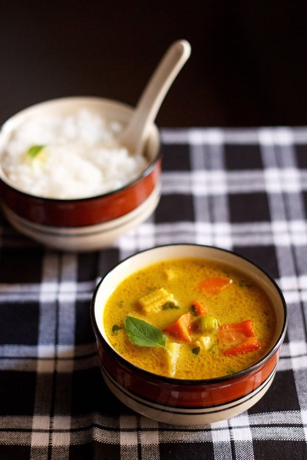 thai yellow curry served in a black rimmed ceramic bowl with a bowl of steamed rice kept in the background.