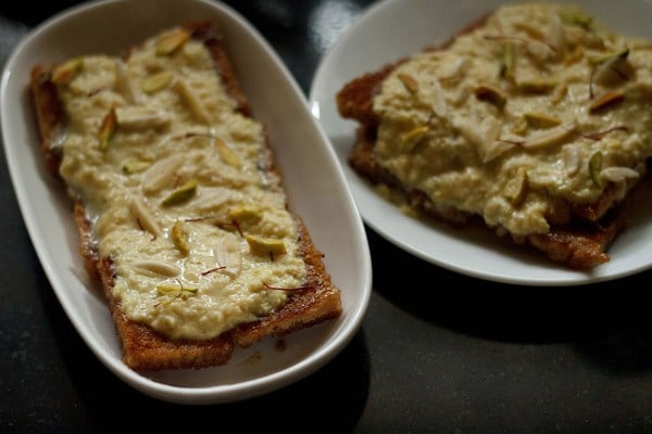 two white serving platters of shahi tukra topped with homemade rabdi, sliced nuts and saffron threads