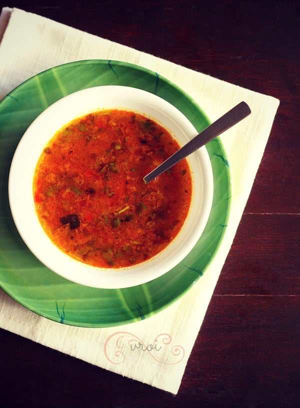 katachi amti served in a white bowl with a spoon in it and placed on a green plate. 