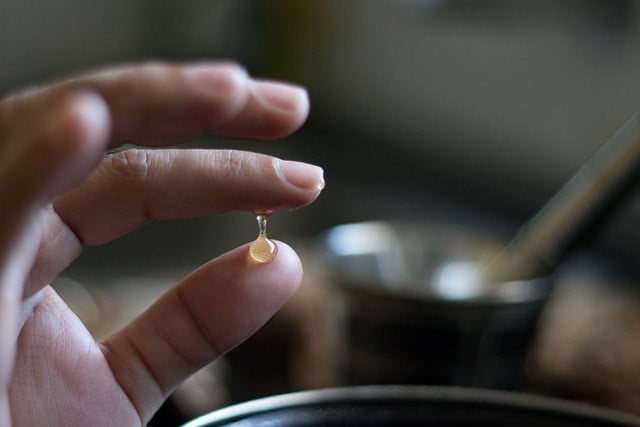 thumb and forefinger pulling apart a dab of caramel syrup to show one thread consistency - making shahi tukra recipe