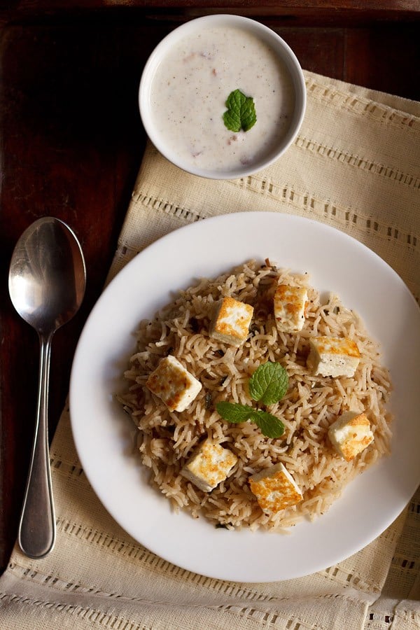 paneer pulao served on a white plate with a side of raita