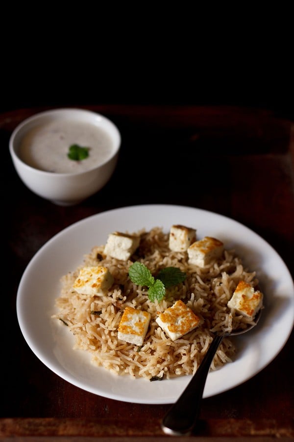 paneer pulao served on a white plate with a side of raita.