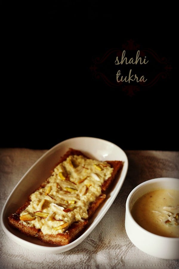 shahi tukda or shahi tukra in a white oblong serving plate with a bowl of homemade rabri, both garnished with sliced nuts and saffron threads.